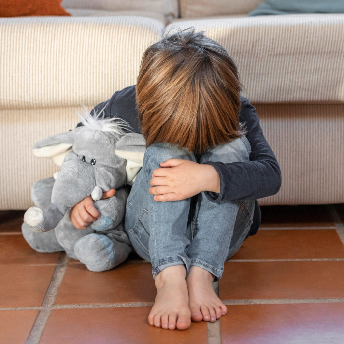 Upset young boy sat on floor holding teddy elephant